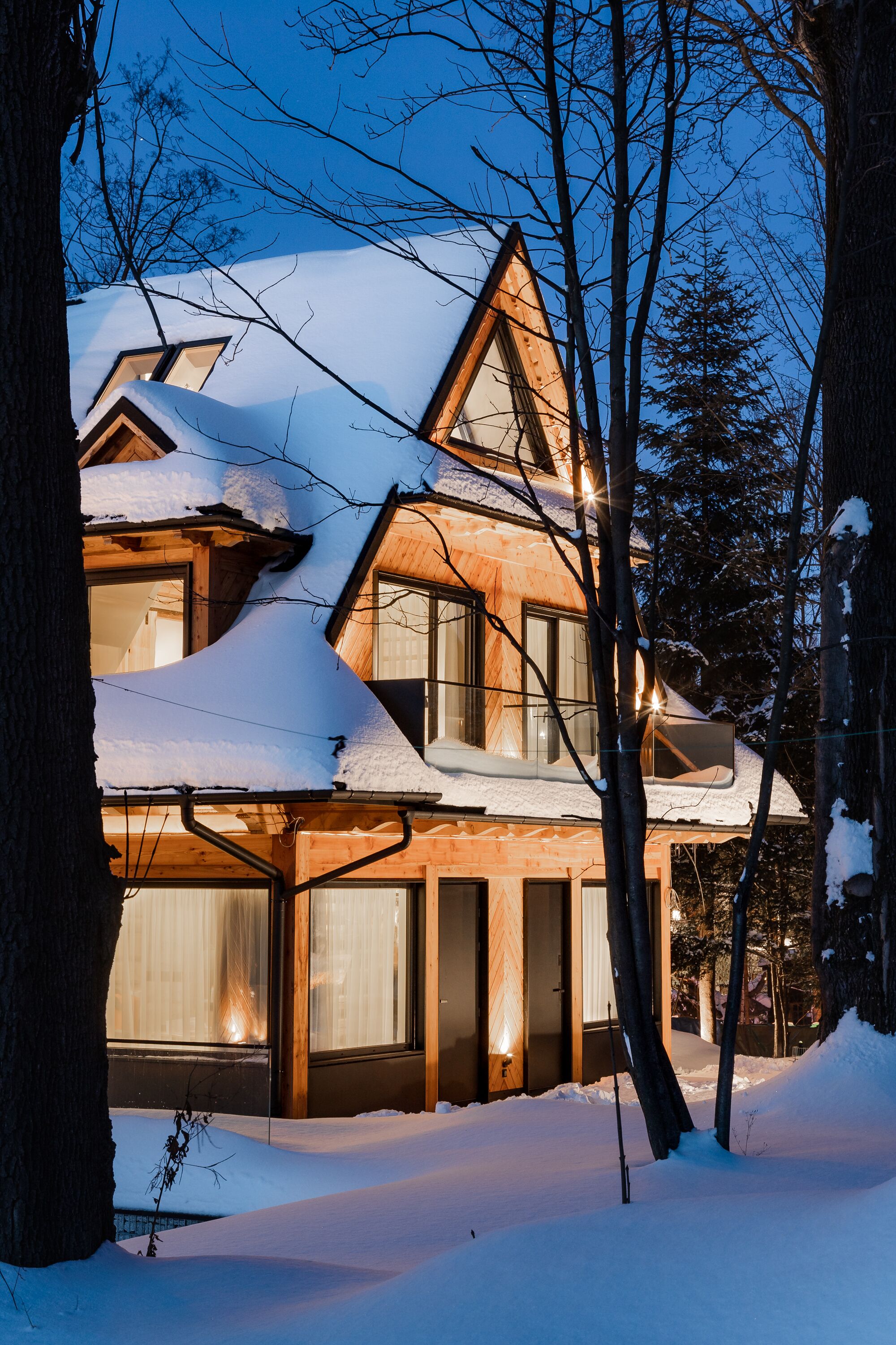 A wooden cabin with a sloped roof, surrounded by snow and trees.