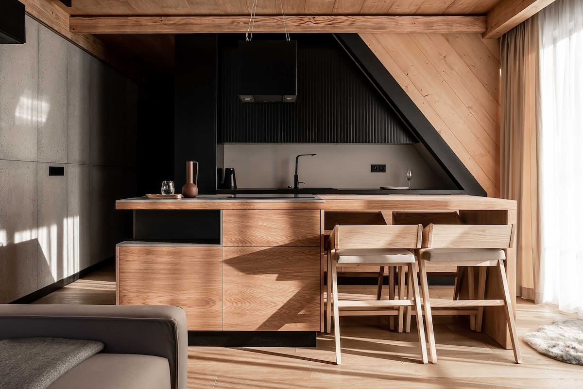 A modern kitchen with a wooden island, bar stools, and a built-in oven.