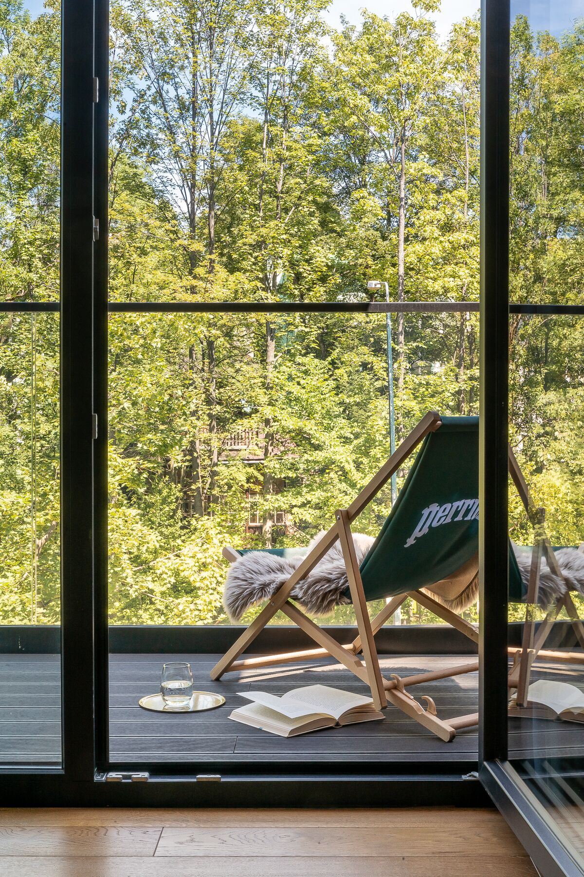 Ein Balkon mit einem grünen Stuhl, einem Glas Wasser und einem geöffneten Buch.