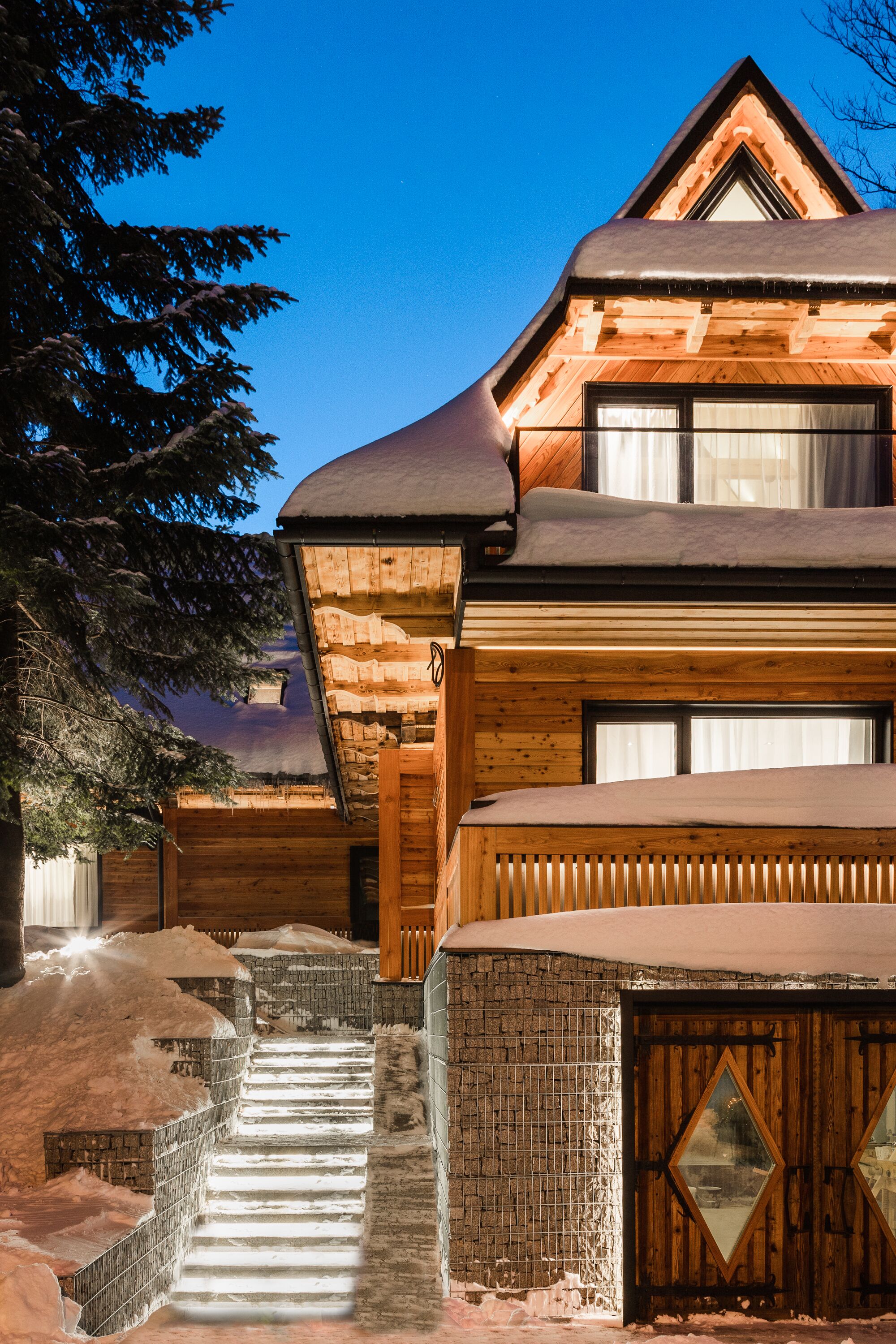 A wooden lodge with a steep staircase leading to the entrance, surrounded by snow.
