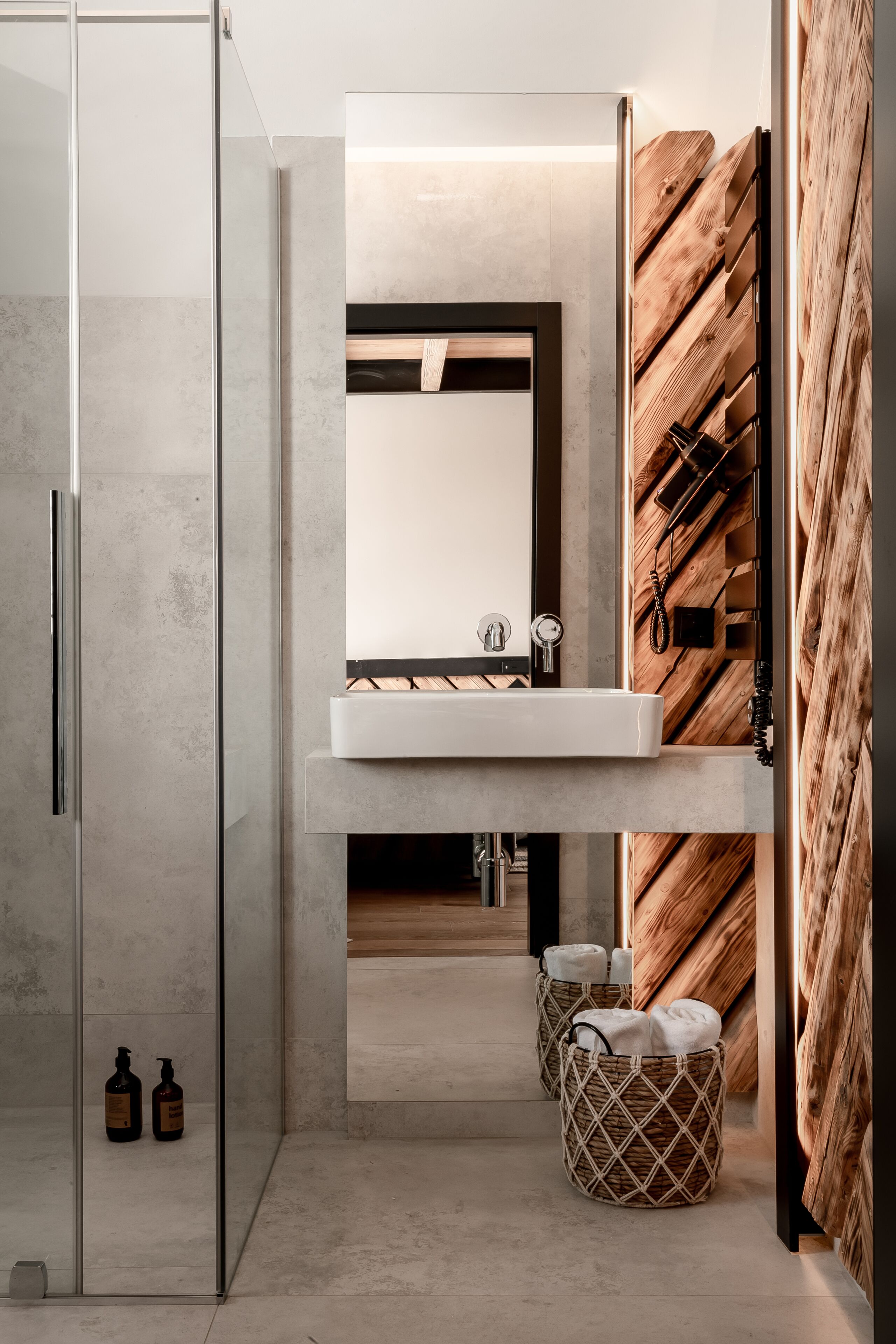 A modern bathroom with a glass shower enclosure, a white sink, and wooden wall panels.