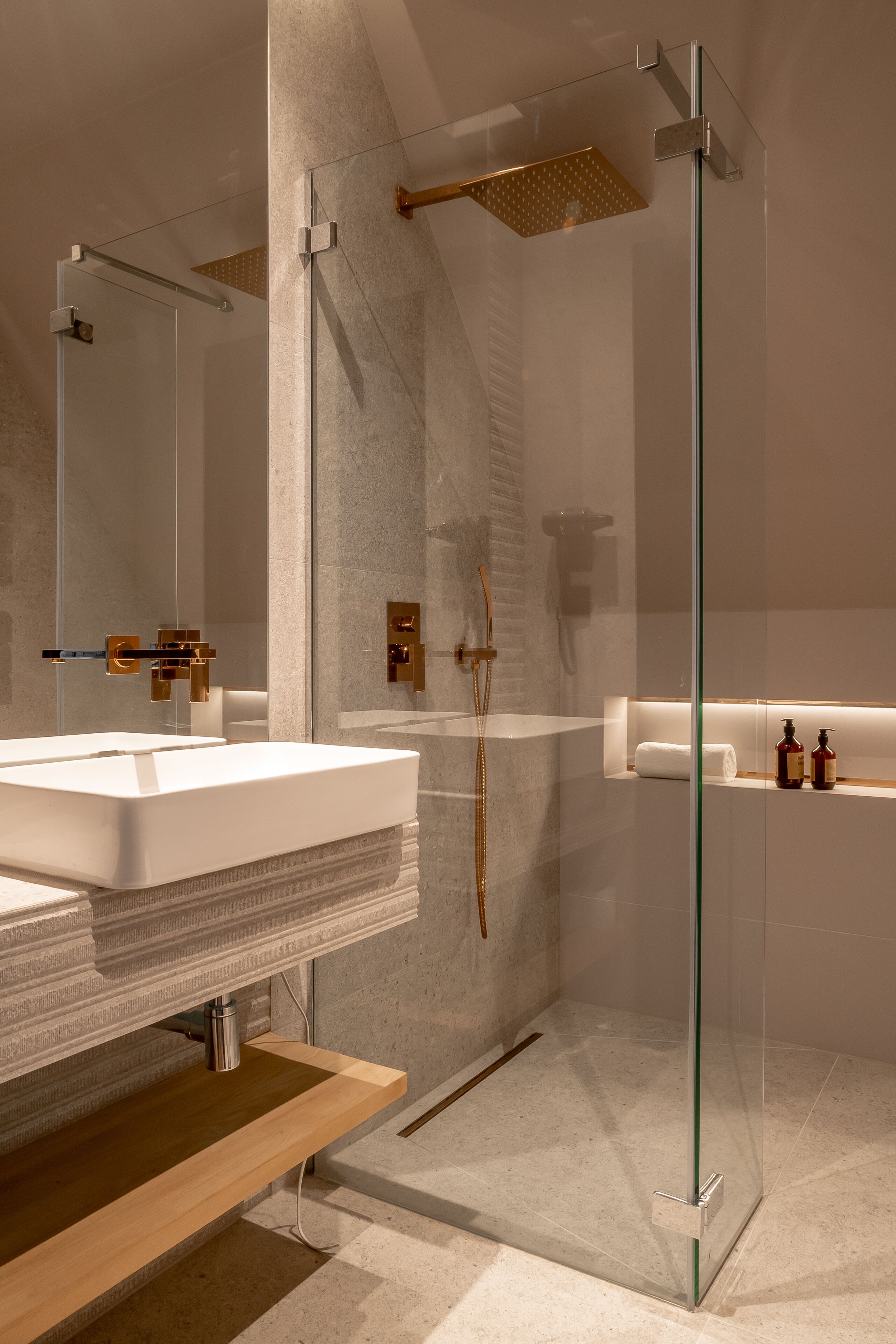 Un baño moderno con ducha envuelta en vidrio, un lavamanos grande de color blanco y un mueble de tocador de madera.