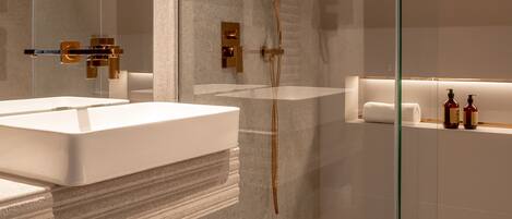 Un baño moderno con ducha envuelta en vidrio, un lavamanos grande de color blanco y un mueble de tocador de madera.
