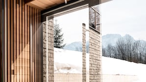 A modern interior with a large glass door leading to a snowy outdoor area, a wooden slatted wall, and a concrete structure. - Villa T Apartments & SPA (Zakopane)