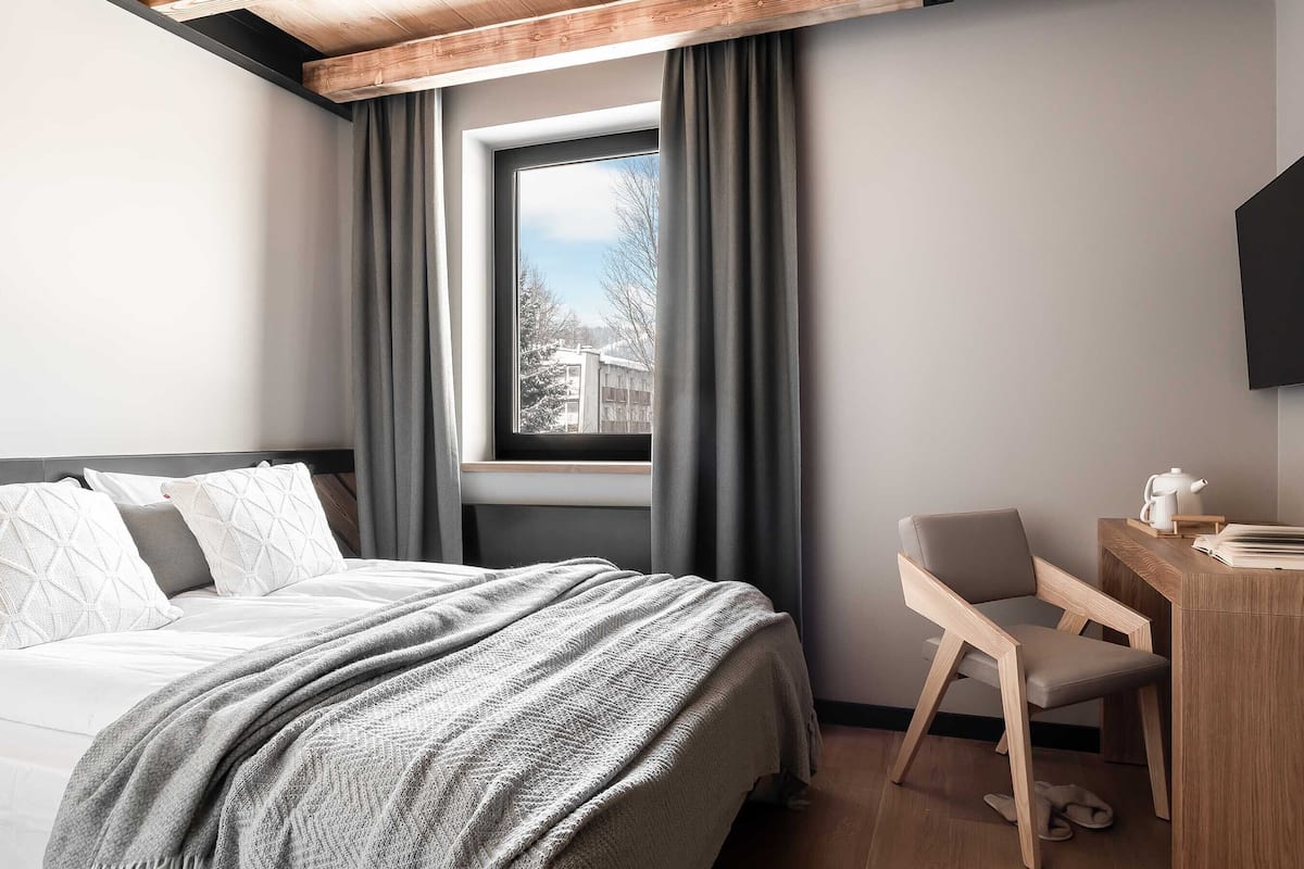 A modern hotel room with a bed, a desk, and a window with curtains.