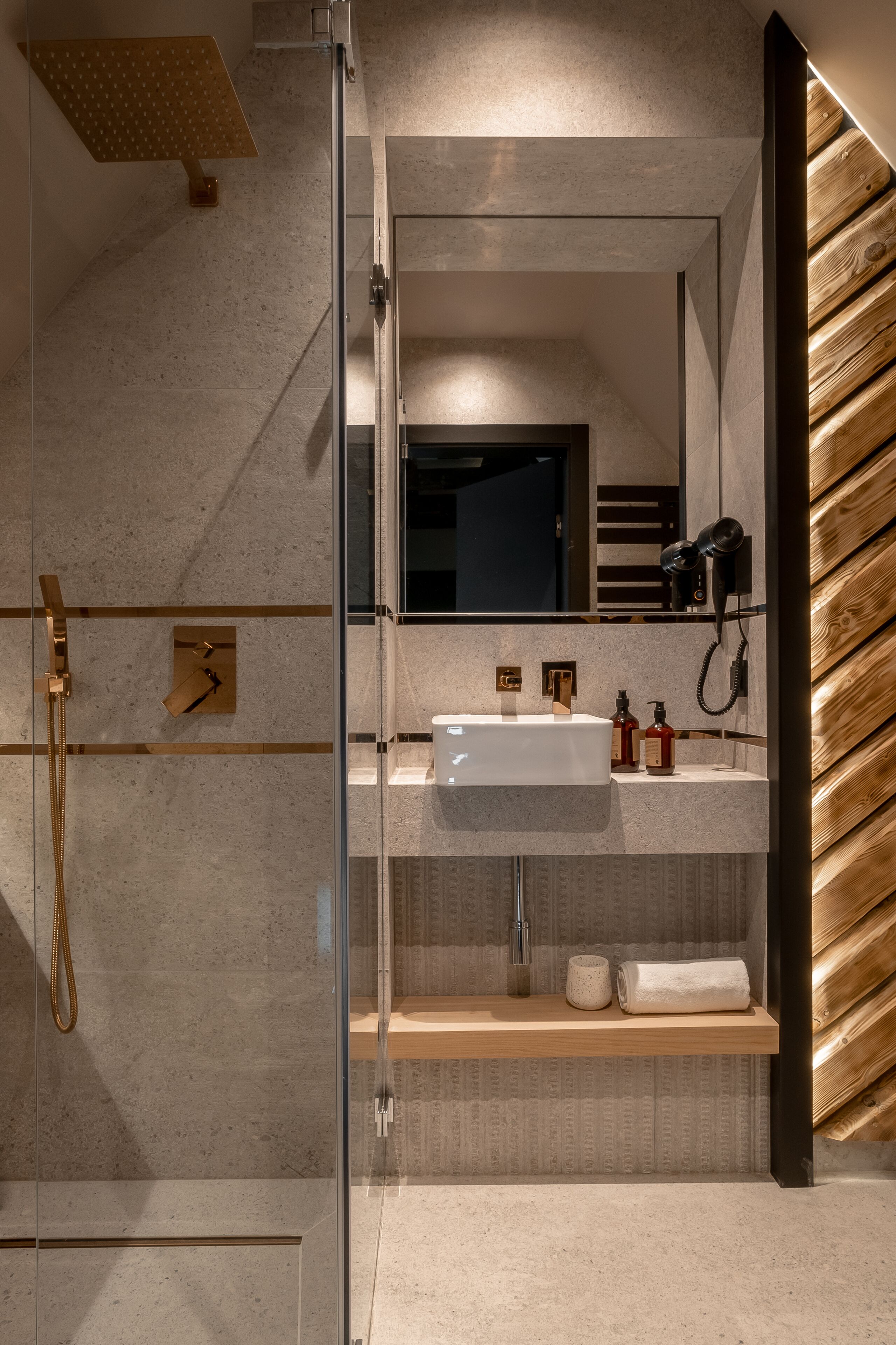 A modern bathroom with a glass-enclosed shower, a vanity with a mirror, and a wooden shelf.