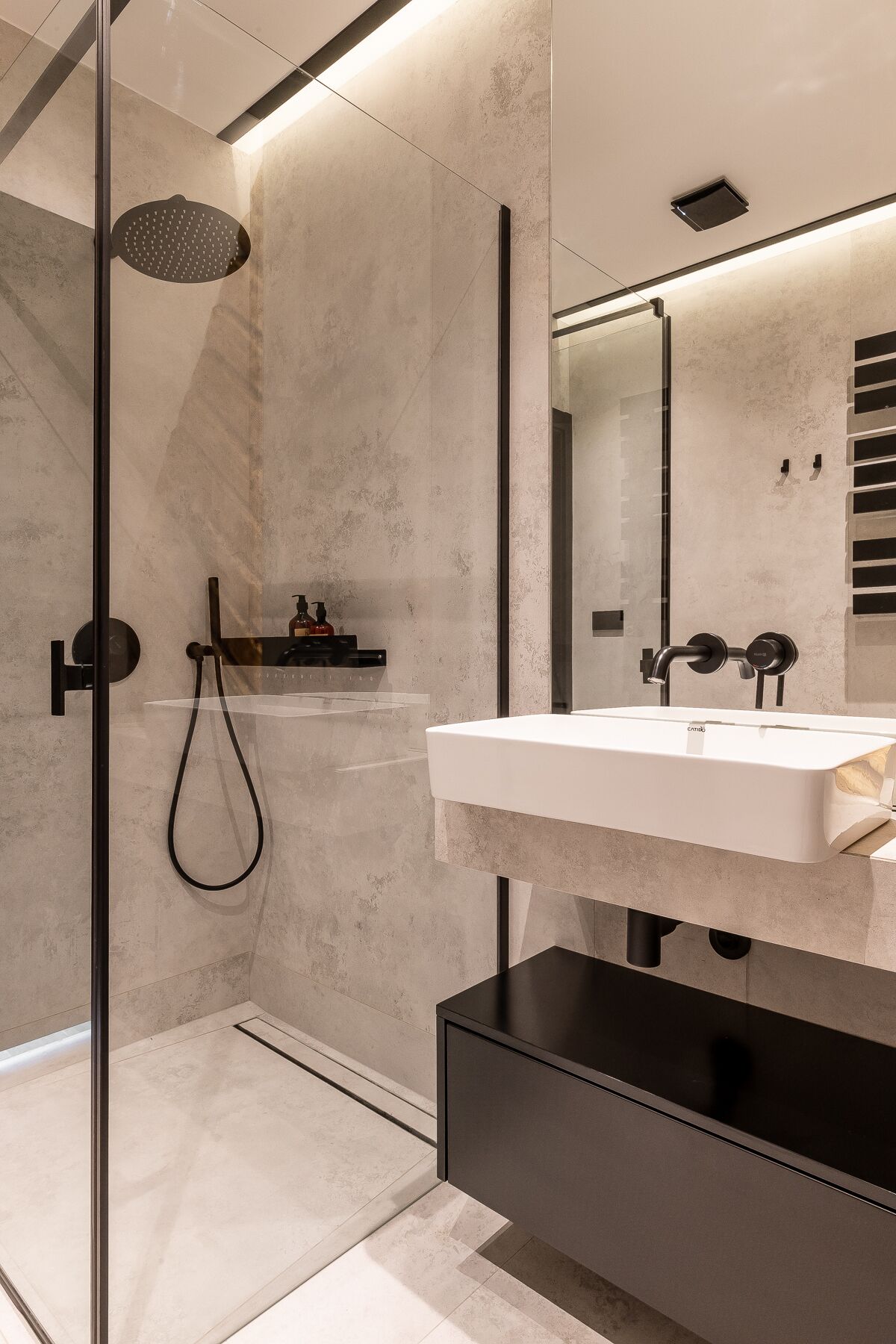 A modern bathroom with a glass-enclosed shower, a white sink with a black countertop, and a large mirror.