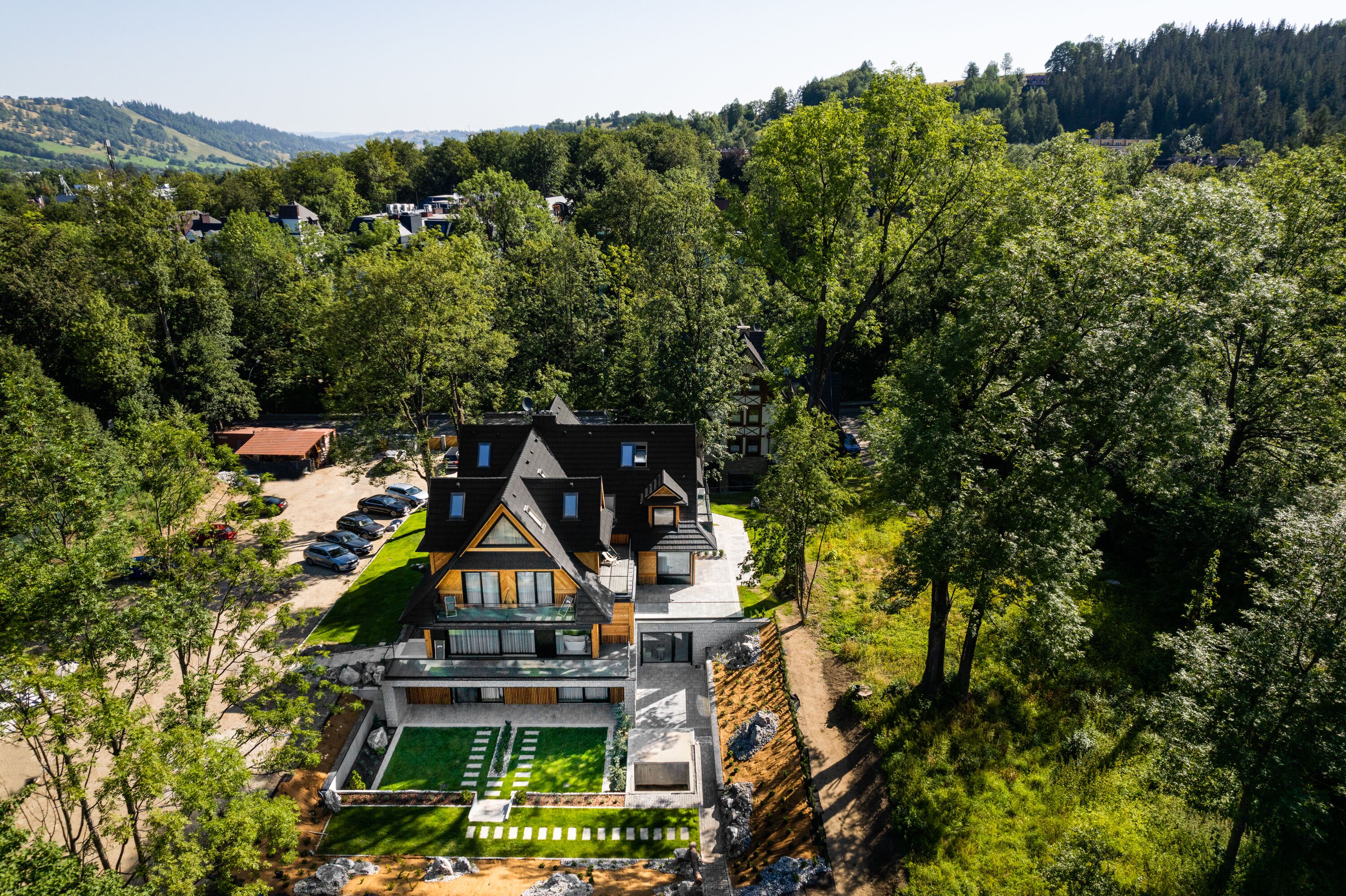 A modern house with a large front yard, a tennis court, and a swimming pool.