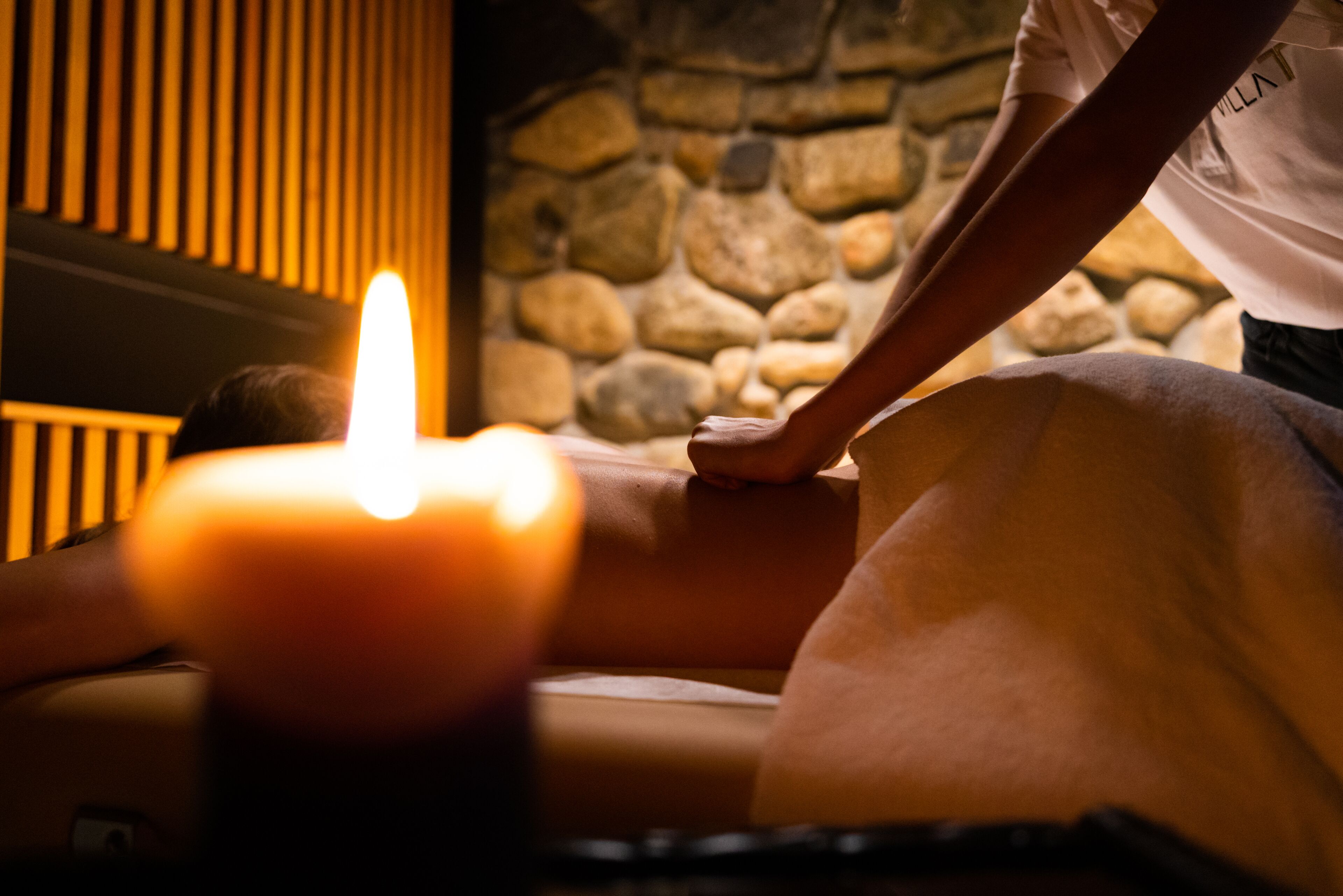 A massage therapy session with a candle in a stone-walled room.
