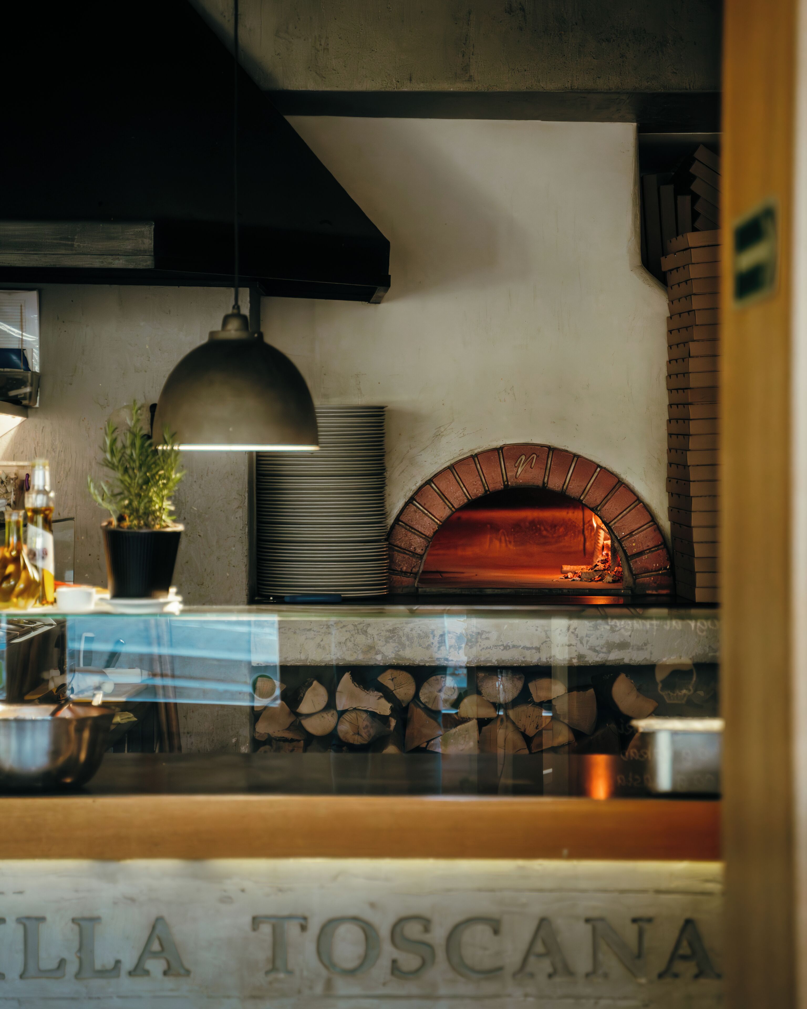 Un horno de ladrillo, una planta en maceta y una encimera de metal con la inscripción 'ILLA TOSCANA'.