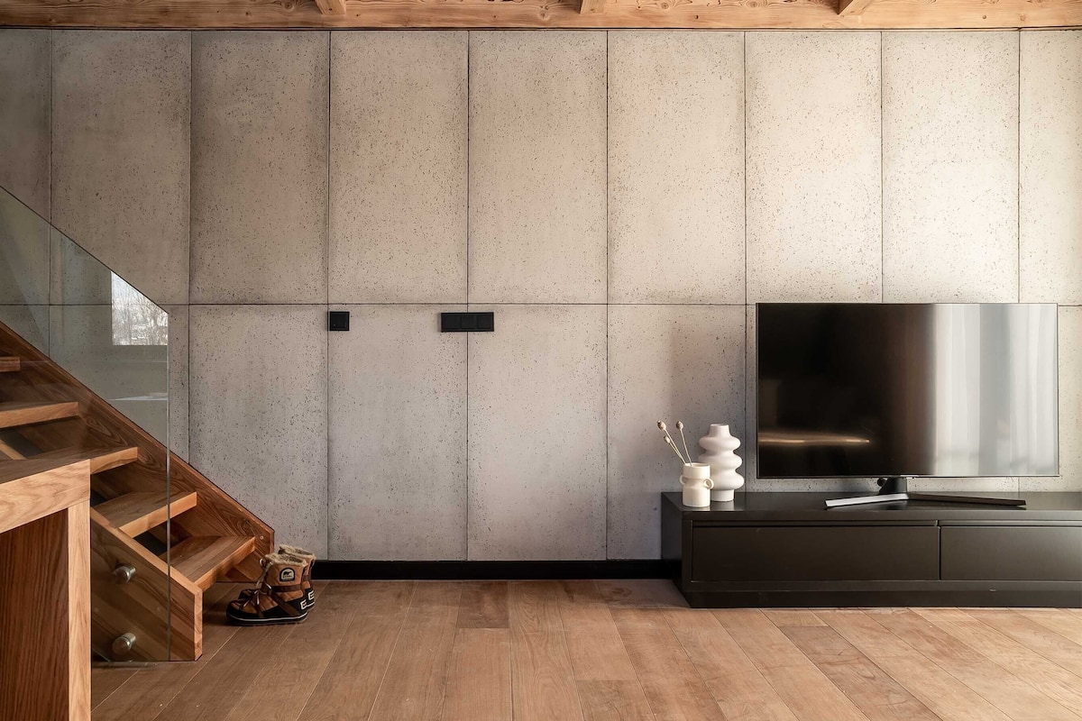 A modern living room with a wooden staircase, a flat-screen TV, and a minimalist design.