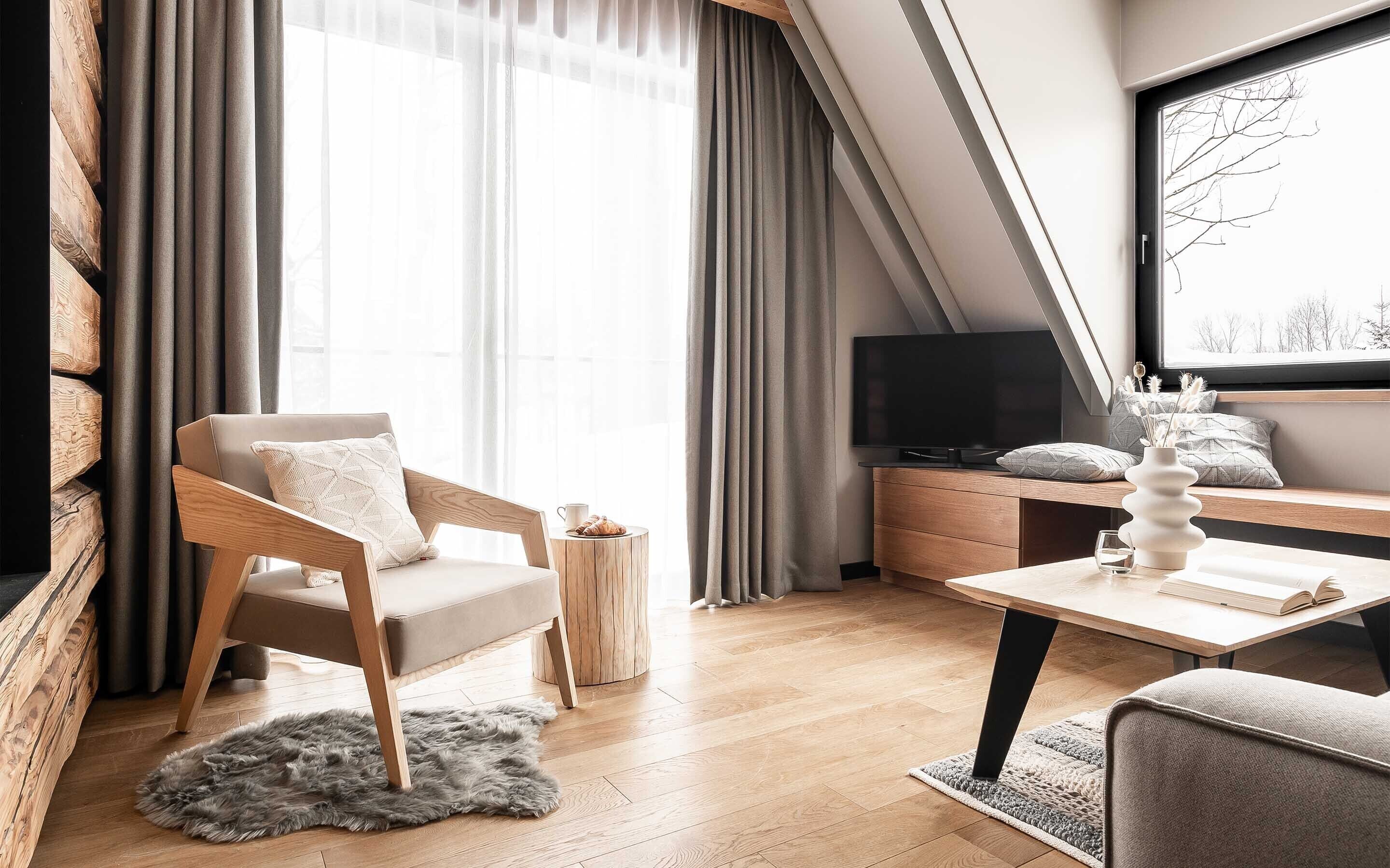 Ein modernes Wohnzimmer mit einer Couch, einem Couchtisch, einem Fernseher und einem Fenster mit Vorhängen.