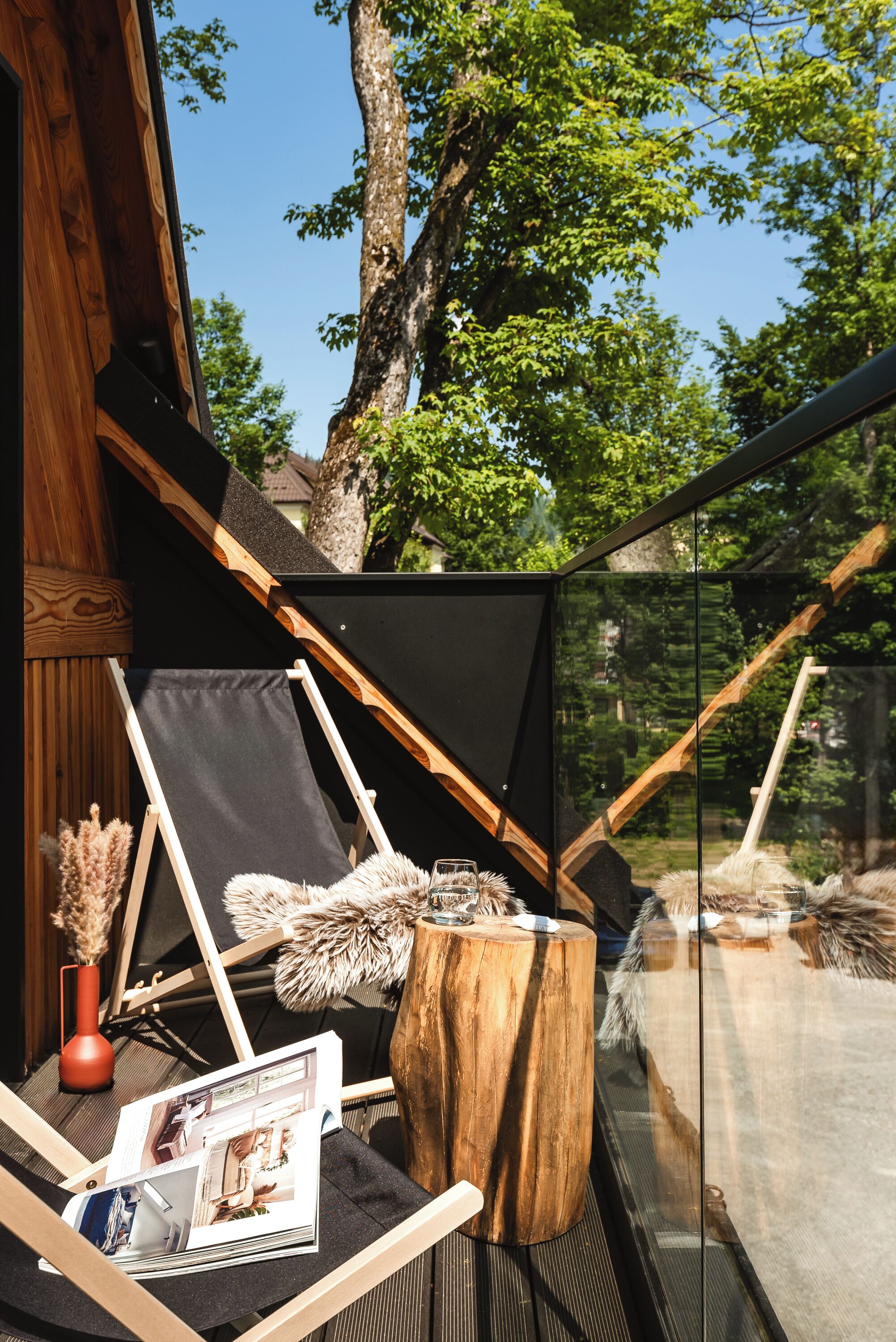 A wooden deck with a glass enclosure, a black awning, and a wooden stool.