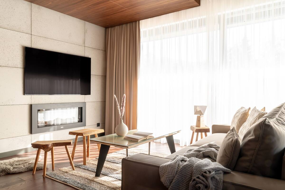 A modern living room with a flat-screen TV mounted on the wall, a fireplace, a sofa, and a coffee table.