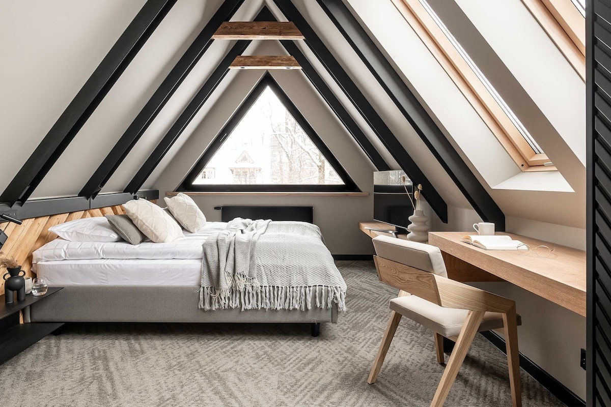 A bedroom with a sloped ceiling, a bed, a desk, and a window.