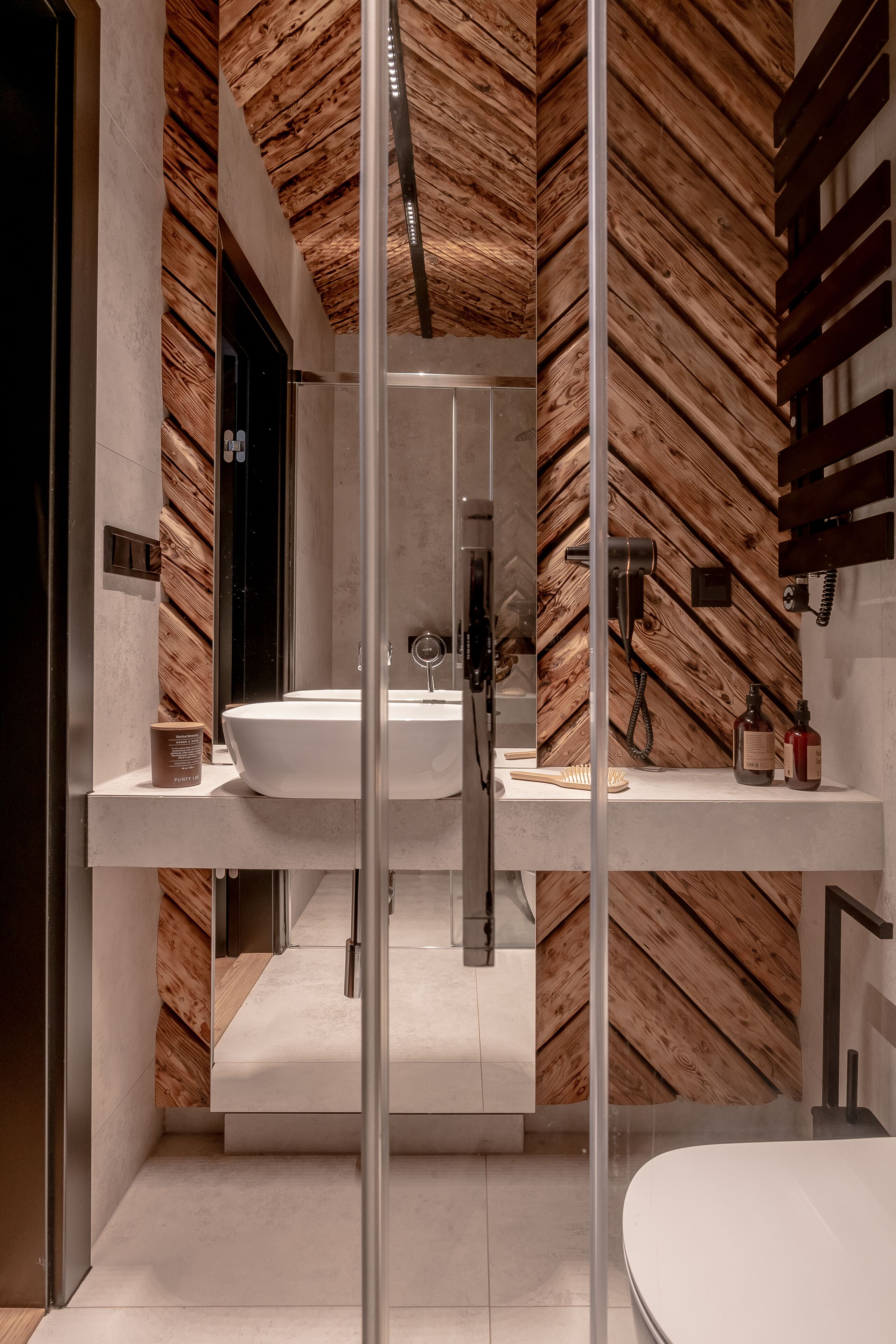 Une salle de bain moderne avec un mur décoré d’un motif en chevrons en bois, un grand lavabo blanc et une douche séparée par des parois en verre.