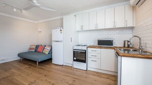 A compact kitchen with white cabinets, a microwave, a stove, and a sink. - Chateau McNally - In the heart of Lancelin (Lancelin)