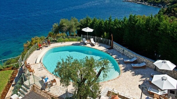 A pool area with a curved design, surrounded by stone walls and furnished with lounge chairs and umbrellas. - Villa Athena (Corfu)