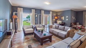 A spacious living room with a checkered floor, a large sofa, a coffee table, and a television. - Villa Athena (Corfu)