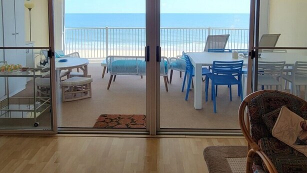 A room with a view of the beach, a dining area with chairs and tables, and a wicker chair in the foreground. - Calypso unit 602, 6201 Coastal Hwy., Ocean City, Maryland 21842 (Ocean City)