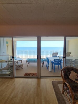 A room with a view of the beach, a dining area with chairs and tables, and a wicker chair in the foreground. - Calypso unit 602, 6201 Coastal Hwy., Ocean City, Maryland 21842 (Ocean City)