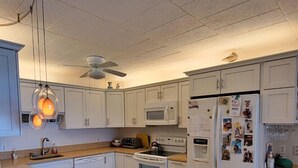 A kitchen with white cabinets, a microwave, an oven, a refrigerator, and a ceiling fan. - Calypso unit 602, 6201 Coastal Hwy., Ocean City, Maryland 21842 (Ocean City)