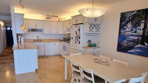 A spacious kitchen with white cabinetry, a central island, and a dining area with white chairs. - Calypso unit 602, 6201 Coastal Hwy., Ocean City, Maryland 21842 (Ocean City)