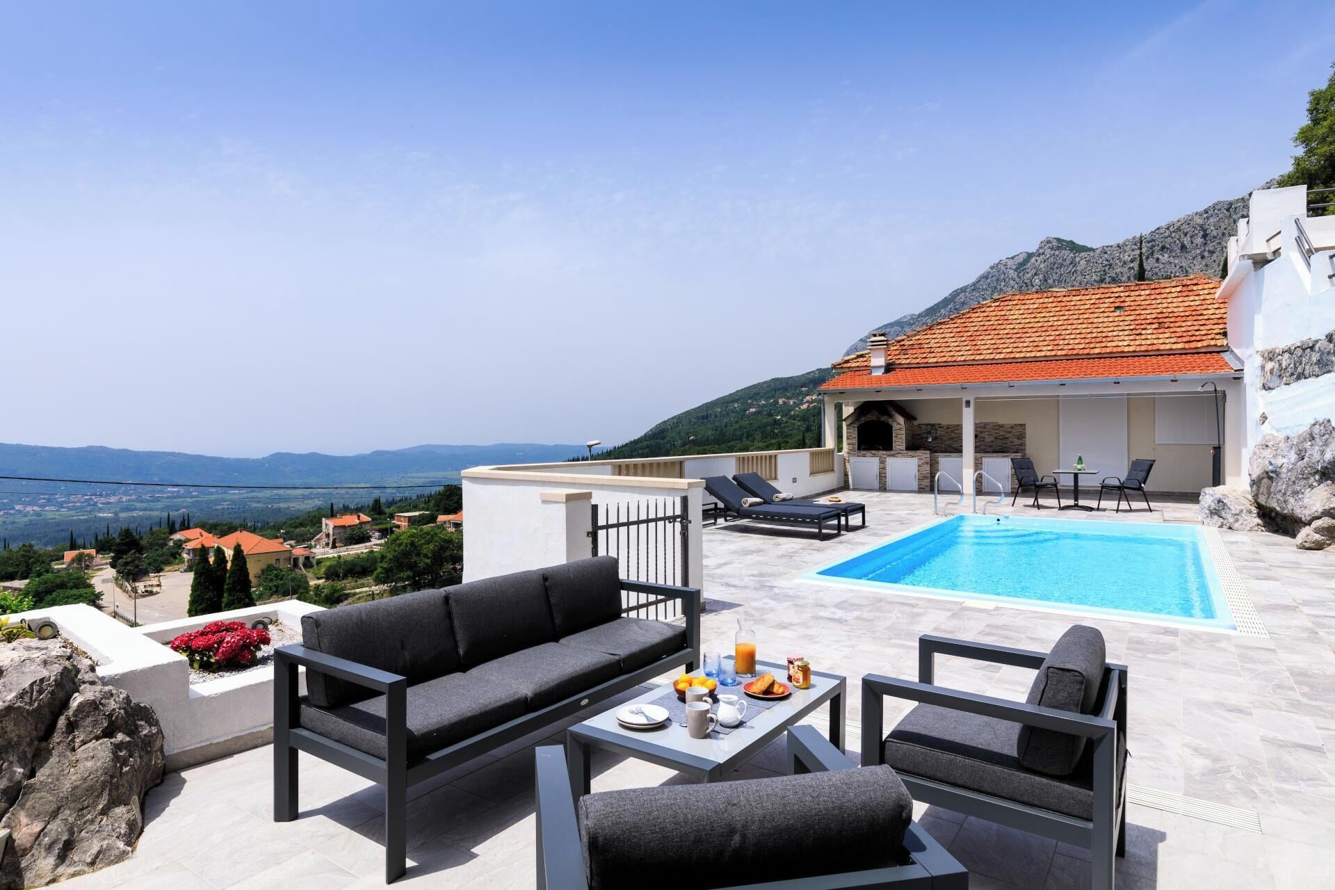 A rooftop pool area with a view of the countryside, a dining table with breakfast items, and outdoor seating.