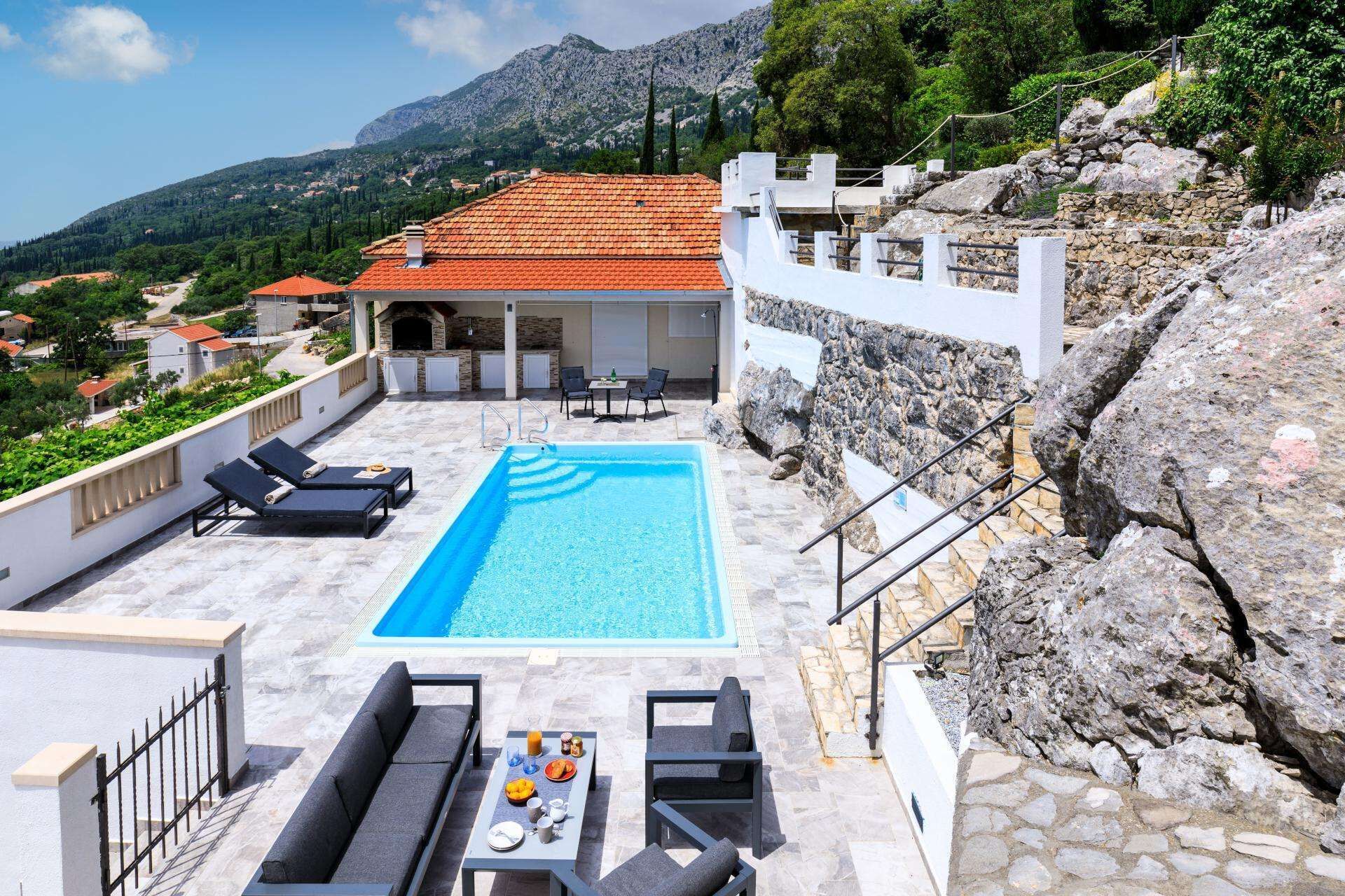 A rooftop pool area with a swimming pool, lounge chairs, and a dining table with breakfast items.