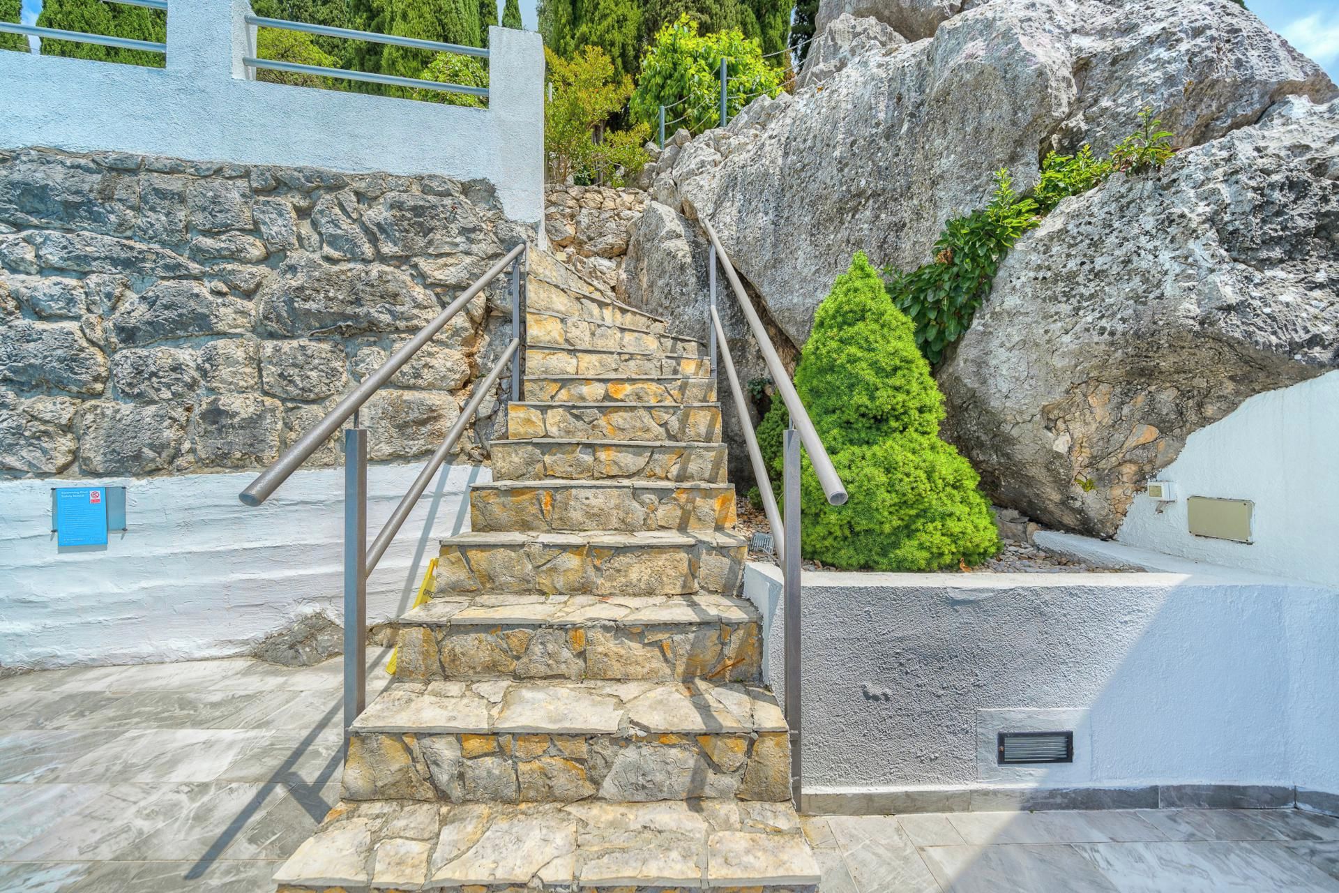 Un escalier en pierre avec des rampes métalliques menant à un bâtiment blanc.