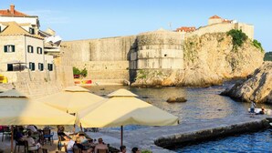 A waterfront dining area with outdoor seating and umbrellas, overlooking a historic stone wall and a body of water. - Duka - One Bedroom Villa, Sleeps 2 (Dubravka, Konavle)