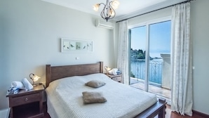 Une chambre dotée d’un grand lit, d’une table de chevet avec une lampe, d’un climatiseur fixé au mur et offrant une vue sur un balcon avec une balustrade.