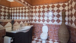 Une salle de bain avec un lavabo blanc, des meubles sombres, des toilettes blanches et un vase décoratif.