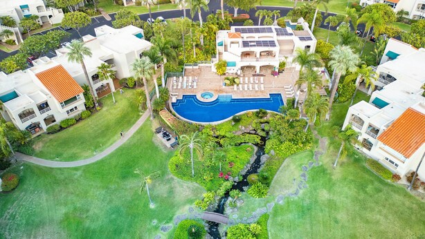 Luchtbeeld van een resort met een centraal zwembad, weelderige beplanting en meerdere gebouwen met balkons.