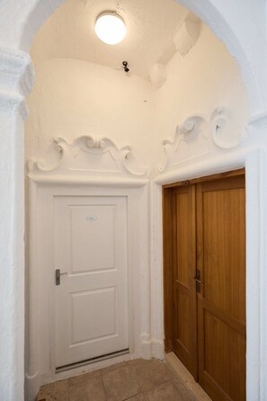 A white door with a small window above it, a wooden door to the right, and a tiled floor.