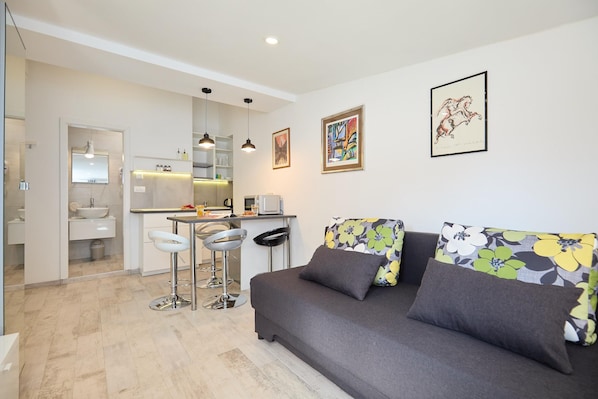 A modern living area with a sofa, a dining table, and a kitchen in the background.