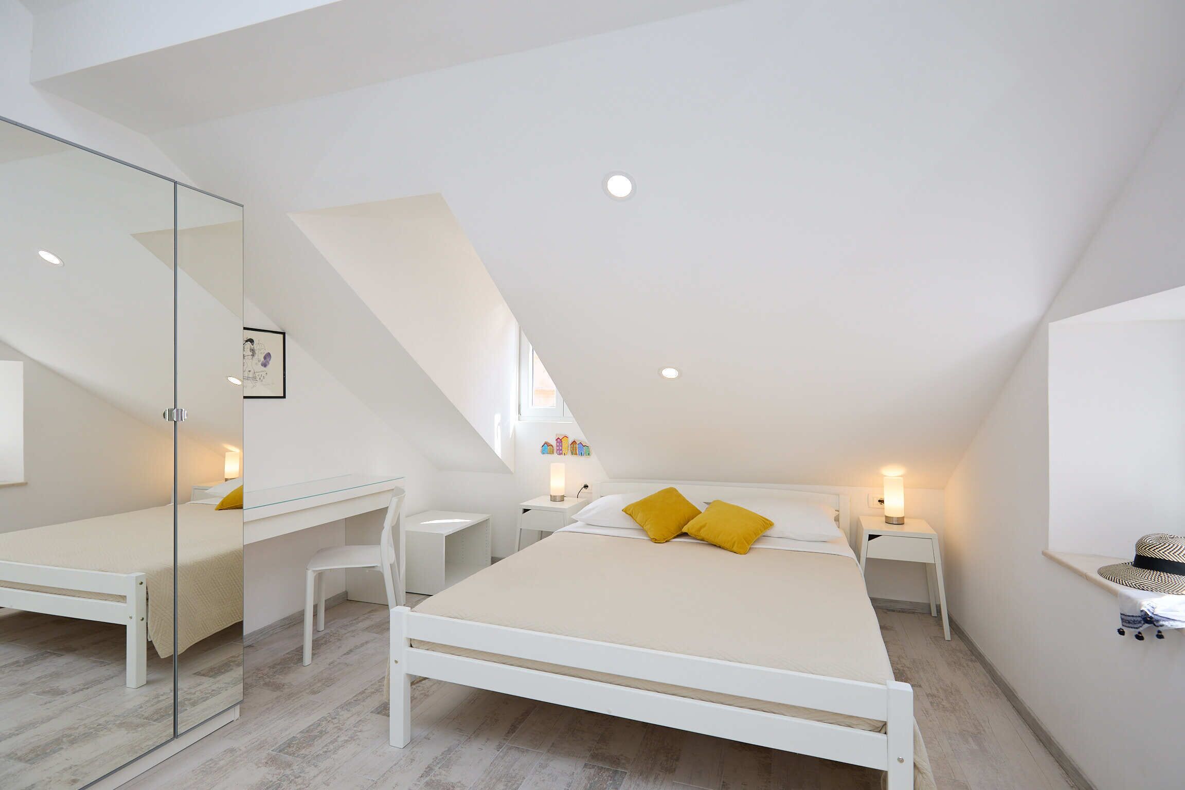 A bedroom with a sloped ceiling, a bed with yellow pillows, a desk, and a mirror.