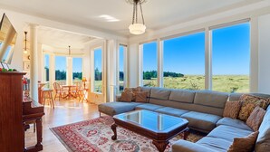 A spacious living room with a large sectional sofa, a wooden coffee table, and a red patterned rug. There is a piano and a dining area visible in the background. - PICKLEBALL! Two hot tubs, ocean views, 2 Homes, 8 Bedrooms, RecRooms (K&KGst) (Long Beach)