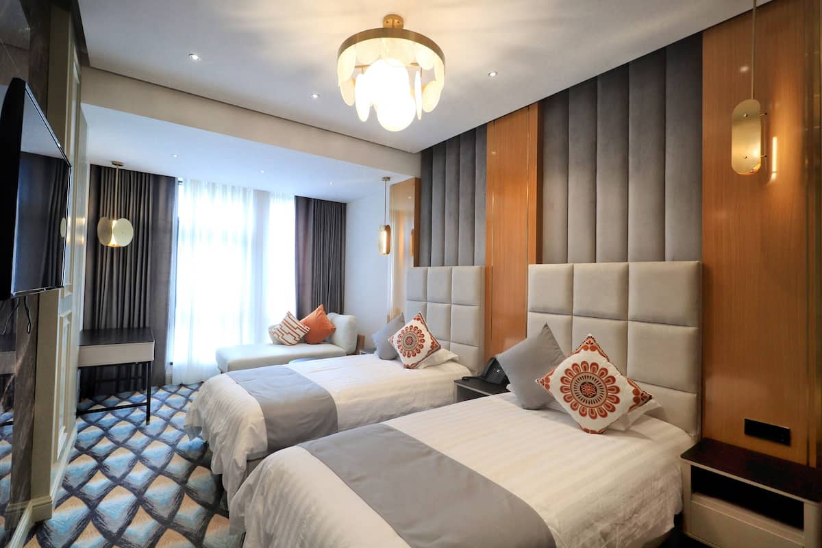 A hotel room with two beds, a television, a desk, and a large window with curtains.