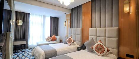 Habitación de hotel con dos camas, televisión, escritorio y un ventanal con cortinas.