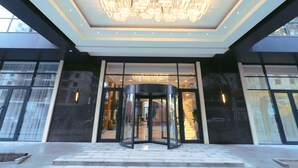 L’entrée d’un hôtel, avec une porte tournante, un grand lustre et une façade en verre.