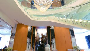 Un hall d’entrée avec un escalier en verre, un grand lustre et des espaces aménagés pour s’asseoir.