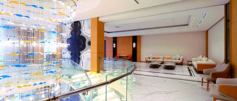 A modern lobby with a glass railing, a seating area with sofas, and a unique fish sculpture installation.