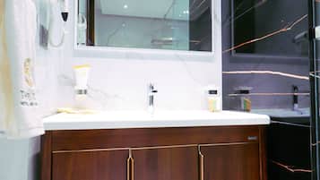 A modern bathroom with a marble vanity, a large mirror, and a dark tiled wall.