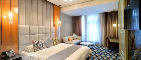 A hotel room with a large bed, a sofa, a small round table, and a TV.