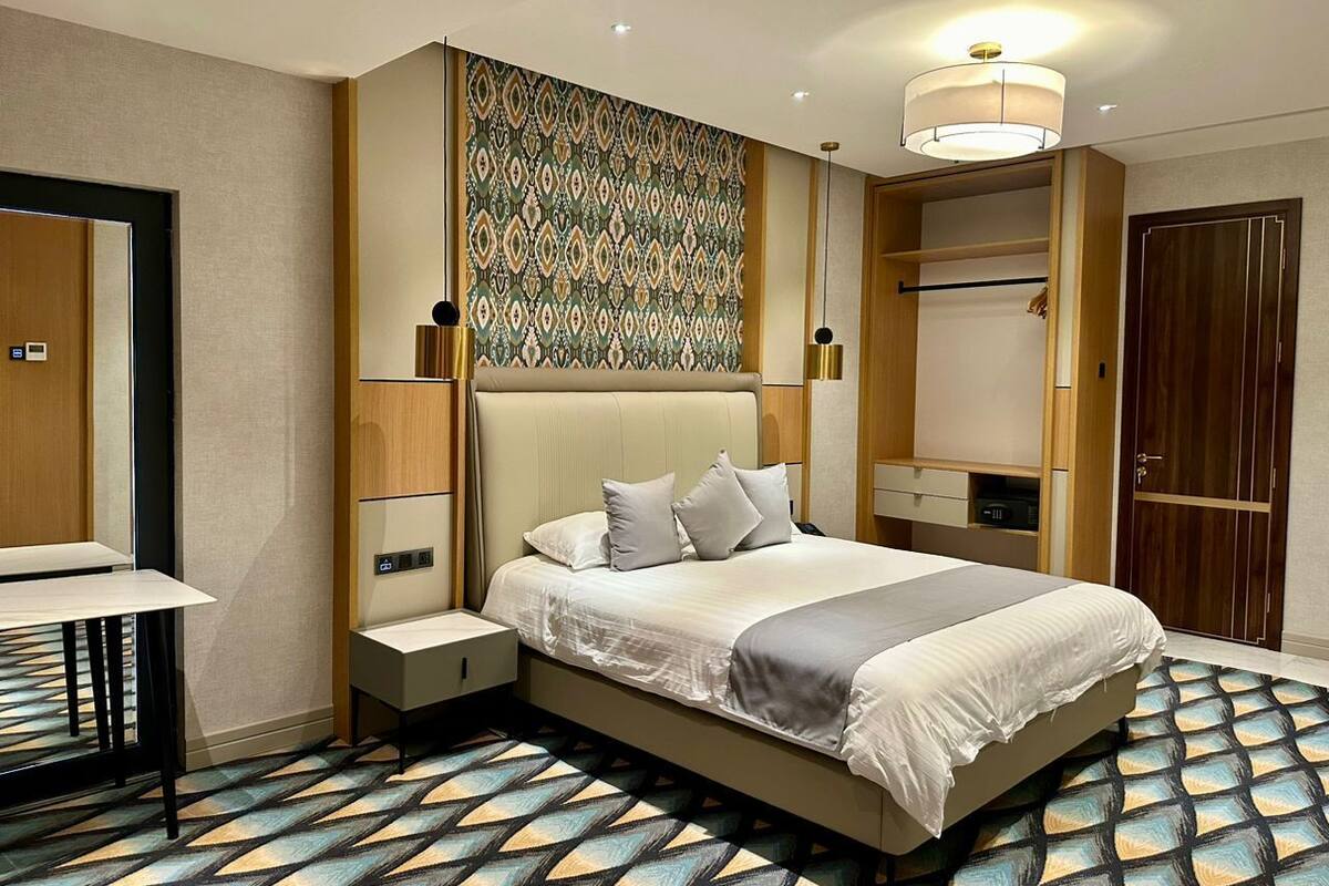A hotel room with a large bed, bedside tables, a wardrobe, and a patterned carpet.