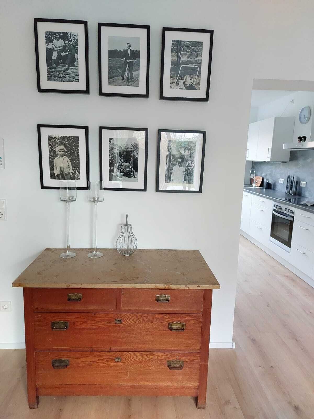 Eine moderne Küche mit weißen Schränken und einem Holzespeisetisch. An der Wand darüber befinden sich sechs gerahmte Schwarz-Weiß-Fotografien.