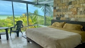 A bedroom with a large window offering a view of the ocean and palm trees.