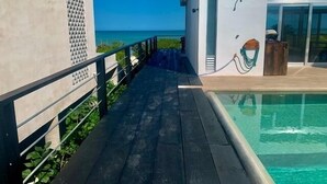 A wooden deck leading to a pool with a clear view of the ocean.