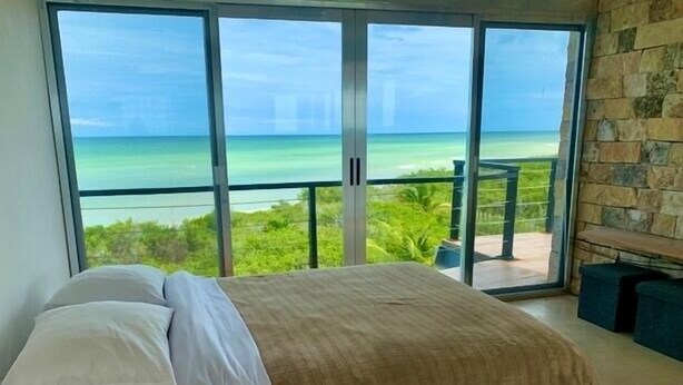 A bedroom with a large bed, a stone wall, and a view of the ocean.